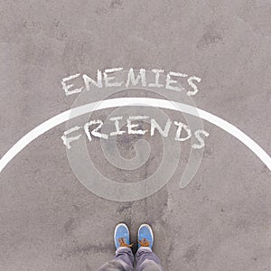 Enemies vs Friends text on asphalt ground, feet and shoes on flo