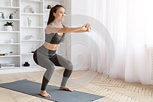 Energetic asian woman performing squats exercise at home