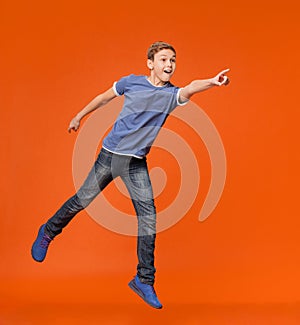 Energetic boy jumping and pointing hand to empty space aside