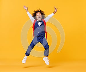 Energetic ethnic stylish schoolboy leaping up against yellow background