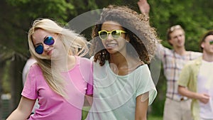 Energetic female couple dancing, smiling for camera, enjoying picnic in park