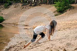 Energetic girl climbing up small hill on sandy beach near river. Little athlete actively spend time close to water.