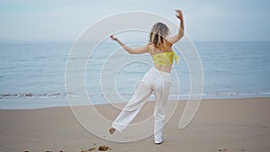 Energetic girl dancing beach looking on beautiful ocean waves. Woman dancer