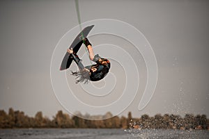 energetic guy jumps high and does somersault on wakeboard over the water