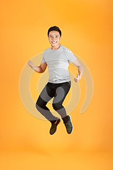 Energetic happy young Asian man in casual clothes jumping, studio shot isolated in orange background