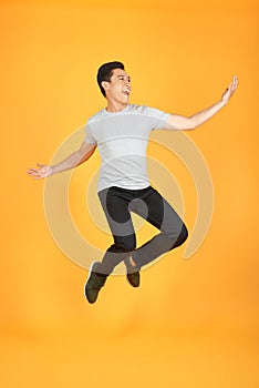 Energetic happy young Asian man in casual clothes jumping, studio shot isolated in orange background