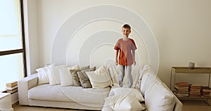 Energetic little boy jumping on comfortable couch in living room