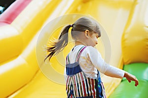 An energetic little girl is playing on a colorful inflatable slide. A child is having fun on an inflatable trampoline. Happy child