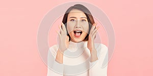 Energetic loud cute beautiful female opening mouth widely, putting hands to mouth, shouting standing isolated over pink background