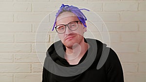 An energetic man with bright purple dreadlocks in glasses shows his tongue