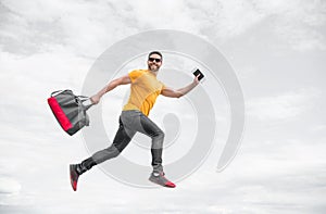 Energetic man running with travel bag midair sky background, vacation