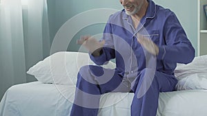 Energetic man sitting on bed in morning smiling and stretching, happy retirement