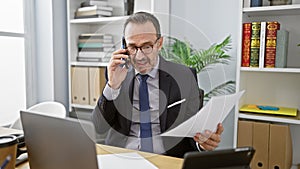 Energetic middle age man with grey hair, immersed in his professional role at the office, confidently talking on a smartphone