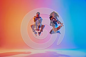 Energetic positive pair, dancers leaping in neon colorful illumination suspended in mid-air against gradient background.