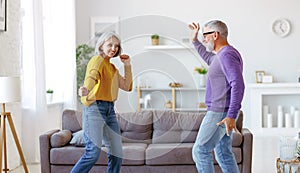 Energetic senior family couple dancing together in living room at home, moving to music