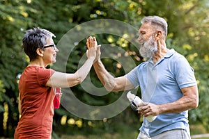 Energetic senior man and woman giving high-five to each other outdoors