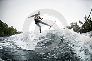 Energetic sports man in black swimsuit rides through the waves on water board