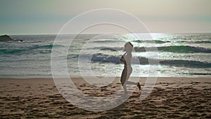 Energetic woman jogging beach at sunrise. Girl spinning on coast feeling happy.