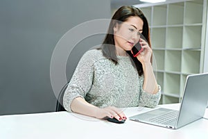 An energetic woman successfully balances business calls and working at a computer in a modern equipped office