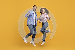 Energetic young black couple jumping mid-air and showing thumbs up