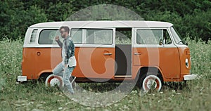 Energetic young guy dancing in front of a retro van, in the middle of nature.