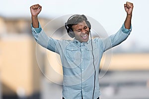 Energetic young man listening to music with headphones and raised his hands.