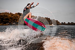 Energetic young woman skillfully jumping over splashing river wave on surf style wakeboard.