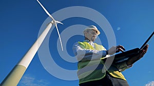 Energetics expert is navigating his computer while standing near a windmill. Renewable alternative energy, environment