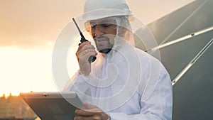 Energetics worker is speaking on a walkie-talkie near a solar panel