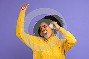 Energized biracial woman sing along, wears wireless headphones, has good mood, isolated on violet background. Happy dark skinned
