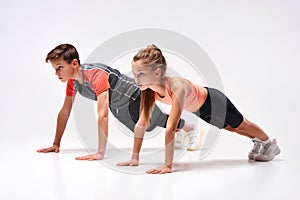 Energizing lives. Full-length shot of teenage boy and girl engaged in sport, looking away while doing push-ups. Isolated