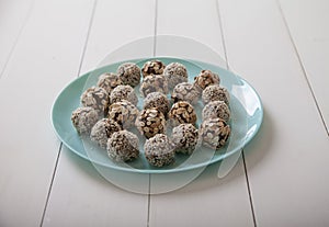 Energy balls of dried fruits and nuts sprinkled with sesame and granola lie on a blue porcelain plate on a white wooden table