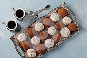 Energy balls of nuts, oatmeal, coconut and cocoa on a metal tray, as well as two cups of coffee on a light blue