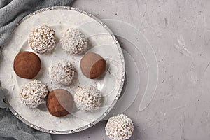 Energy balls of nuts and oatmeals with coconut flakes and cocoa on white plate on gray background, horizontal format