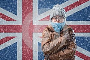 Energy crisis in Europe. Woman in hat, coat and scarf is warming herself. In the background is the flag of UK and a