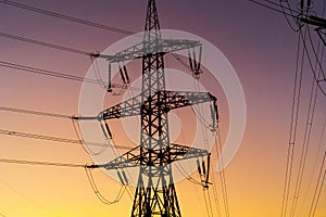 Energy Distribution Network - Electricity Pylons against Orange and Yellow Sunset. Closeup