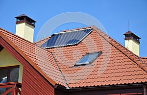 Energy efficiency concept. Closeup of solar water panel heating on red tiled house roof with lightning protection, skylights, photo