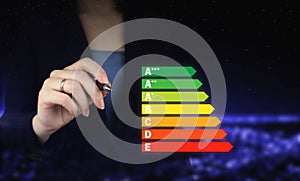 Energy efficiency concept. Hand holding digital graphic pen and drawing digital hologram energy efficiency sign on city dark