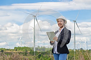Energy engineer female working at wind farm. asian business woman wearing suit holding tablet and clipboard with windmill