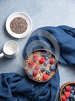 Energy granola with raspberry,  blueberry, chia seeds and vegan milk into coconut bowl on blue background