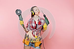Energy handyman woman in gloves, noise insulated headphones, kit tools belt full of instruments holding power saw