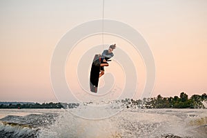 energy man engaged in water sport and jumping on splashing wave on a wakeboard