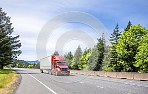 Energy saving design big rig red semi truck transporting cargo in dry van semi trailer moving on the divided highway road with