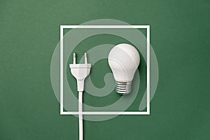 Energy-saving and eco-friendly life. Creative top view flat lay of LED light bulb, electrical plug and white frame with copy space