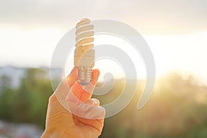 Energy saving fluorescent light bulb, hand holding lamp, evening sunset sky background