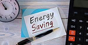 ENERGY SAVING - words on a white sheet on the background of a calculator, alarm clock and pen