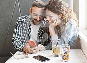 Engaged couple enjoying time together using smartphone - Friends are having fun in a bar with mobile phone