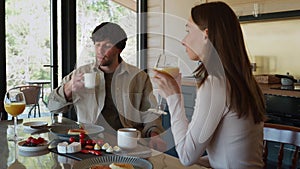 An engaged couple has breakfast together in their new home - a young couple talks while eating and drinking in the