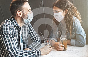 Engaged couple sitting in a caffe bar with surgical masks during the coronavirus pandemic - prevention and social distancing