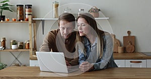 Engaged couple using laptop in kitchen, typing, using online app